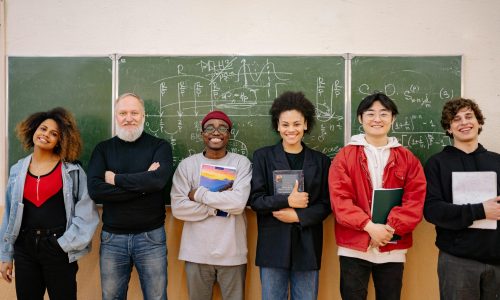 A diverse group of students and a teacher smiling in front of a chalkboard filled with formulas.